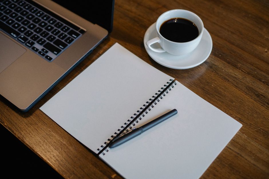 From above of workspace with cup of hot coffee and pen on empty notepad near modern laptop on wooden table